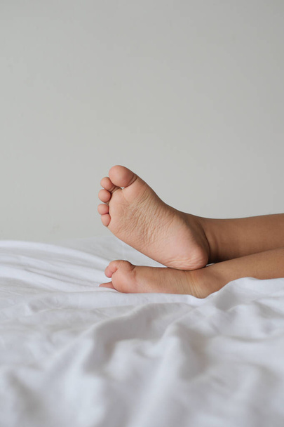 Детские босые ноги на белой кровати . - Фото, изображение