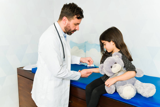Лікар робить аналіз або тестування SPT на алергію на шкіру руки чарівної маленької дівчинки з плюшевим ведмедем
 - Фото, зображення