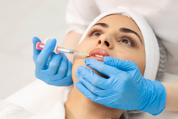 lip augmentation procedure using botox in cosmetology clinic, cosmetologist doctor in gloves makes injection with syringe in the patient's lips, close-up of syringe and needle - Foto, Imagem