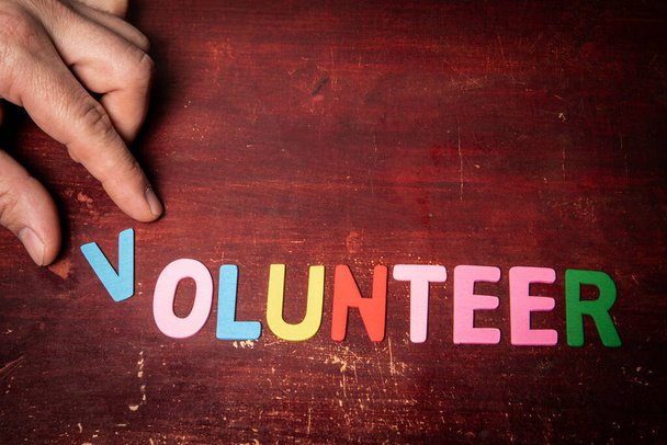 VOLUNTEER. Text from colorful letters on a wooden background. - Foto, imagen