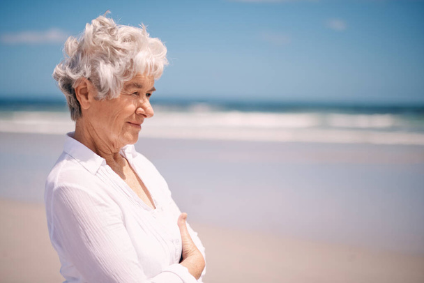 Genießen Sie die frische Meeresluft. Eine Seniorin steht am Strand - Foto, Bild