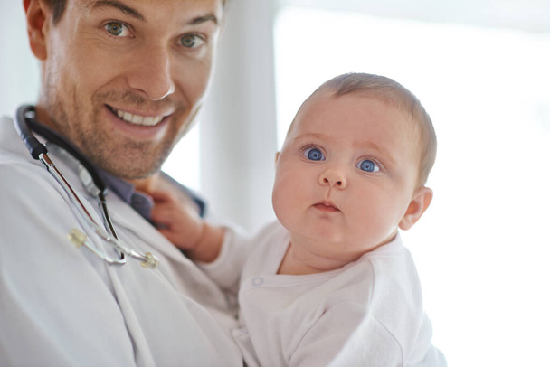 Πολύτιμη ζωή. Πορτρέτο ενός όμορφου άντρα γιατρού που κρατάει ένα αξιολάτρευτο μωρό - Φωτογραφία, εικόνα