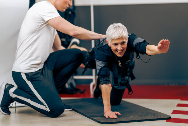 Starsza kobieta trenuje EMS z trenerem personalnym na siłowni. - Zdjęcie, obraz