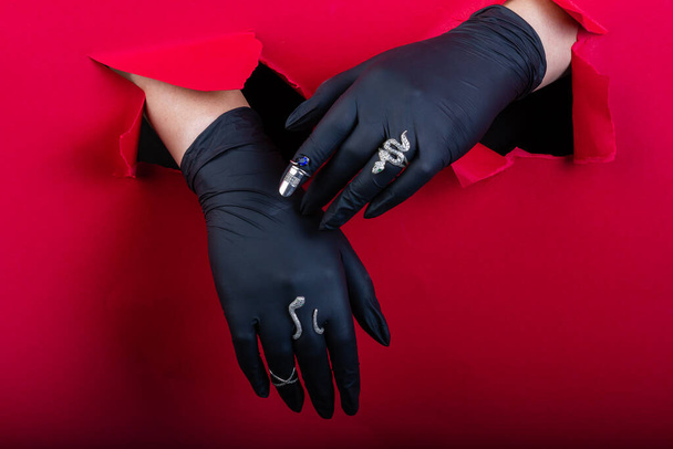 Gloved hands with silver jewelry breaking a paper wall. Red wall background. - Foto, Imagem
