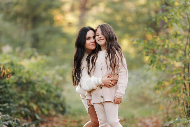Mothers day. Beautiful smiling young mom with teen daughter are hugging and looking at camera outdoors in the autumn park. Family day. Idyllic stylish family of two communicate alone. happy childhood - Foto, imagen