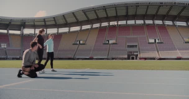 Három fiatal készül versenyezni a futópályán egy üres stadionban - Felvétel, videó