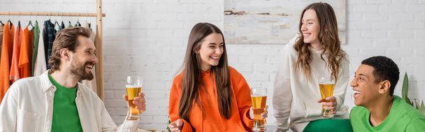 cheerful multiethnic friends holding glasses of beer while smiling in living room, banner  - Foto, Imagem