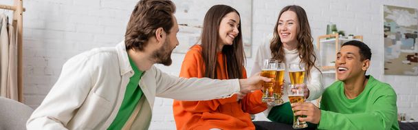 cheerful interracial friends clinking glasses of beer in living room, banner  - Foto, Imagem