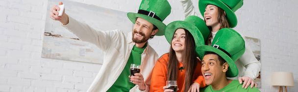 cheerful bearded man taking selfie with interracial friends holding glasses of dark beer on Saint Patrick Day, banner  - Photo, image