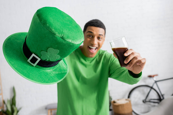 heureux homme afro-américain tenant un verre de bière sombre et chapeau vert le jour de la Saint Patrick - Photo, image