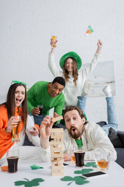 Excited interracial friends playing wood blocks game near beer and whiskey at home  - Fotoğraf, Görsel