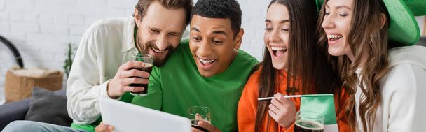 Cheerful interracial friends with beer using digital tablet while celebrating saint patrick day, banner  - Fotoğraf, Görsel
