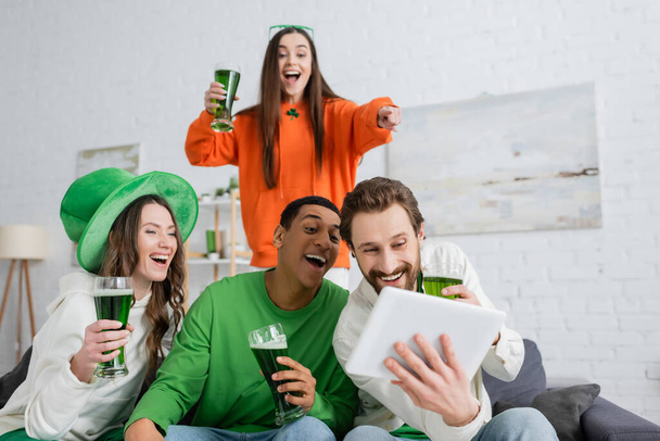 Positive interracial friends with green beer using digital tablet during saint patrick day  - Foto, imagen