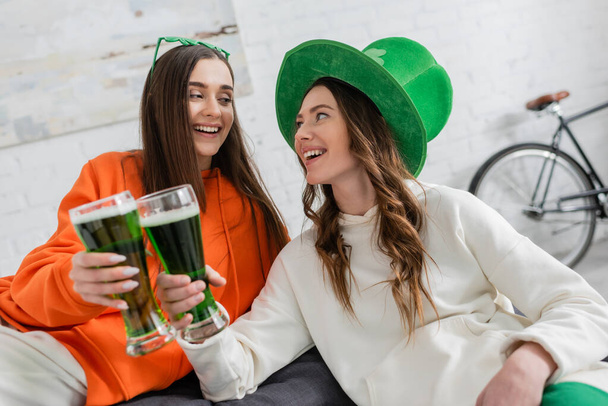 Uśmiechnięte młode kobiety brzęczące zielonym piwem świętując dzień świętego Patryka  - Zdjęcie, obraz