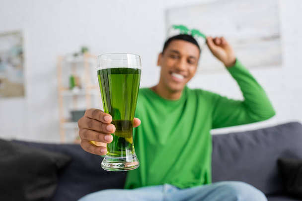 Blurred african american man holding green beer at home  - Фото, изображение