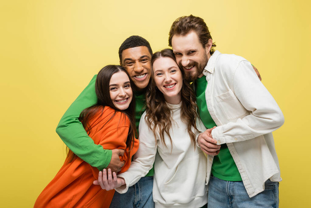Cheerful multiethnic friends hugging isolated on yellow  - Foto, afbeelding