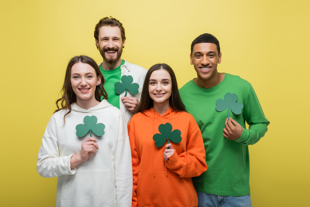 Happy multiethnic people holding paper clover isolated on yellow  - Fotografie, Obrázek