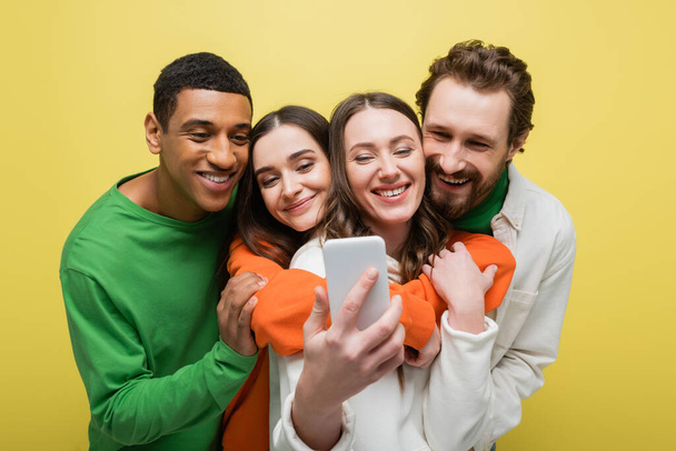 Positive interracial friends taking selfie on smartphone isolated on yellow  - Φωτογραφία, εικόνα