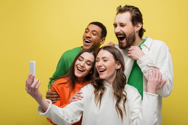 Positive multiethnic friends using mobile phone isolated on yellow  - Foto, immagini