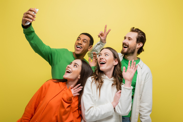 Amigos multiétnicos que tienen videollamada en smartphone aislado en amarillo  - Foto, imagen