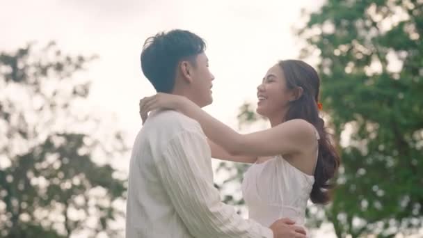 Sweet lovers arm around shoulder hug neck face to face talking at outdoor nature. Trust true love smile happy asia people in casual bride groom white dress begin family life just married young couples - Footage, Video