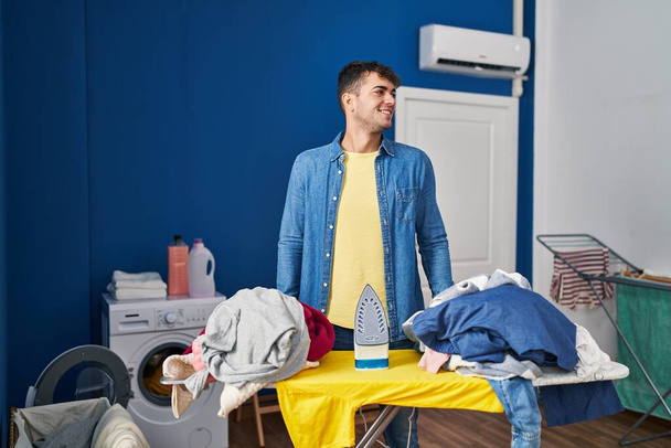 Young hispanic man ironing clothes at home looking to side, relax profile pose with natural face and confident smile.  - Foto, Imagem