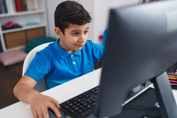 Чарівний іспаномовний хлопець студент, використовуючи комп'ютер, сидячи на столі в класі
 - Фото, зображення