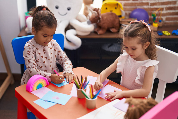Двое детей-дошкольников сидят за столом и рисуют на бумаге в детском саду - Фото, изображение