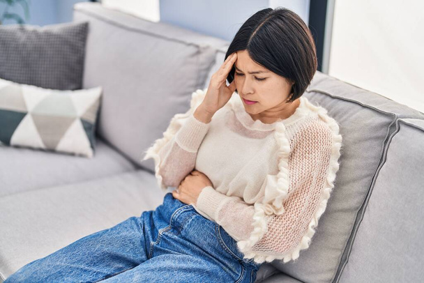 Young chinese woman stressed sitting on sofa at home - Zdjęcie, obraz