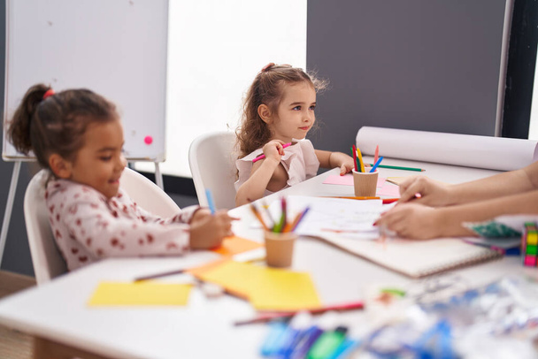 Двое детей-дошкольников сидят за столом и рисуют на бумаге в классе - Фото, изображение