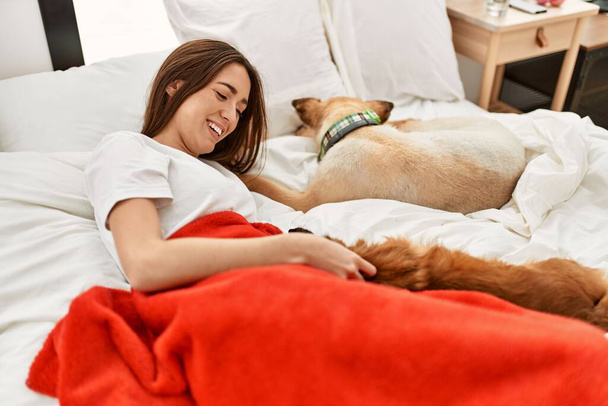 Jeune femme hispanique étreignant chien couché sur le lit dans la chambre - Photo, image