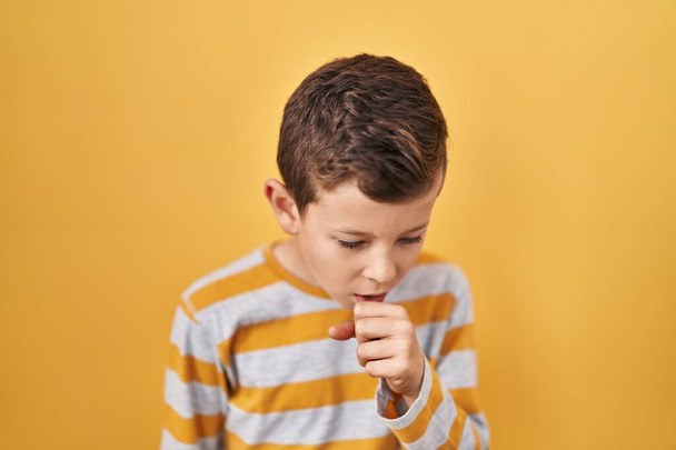 Young caucasian kid standing over yellow background feeling unwell and coughing as symptom for cold or bronchitis. health care concept.  - Photo, image