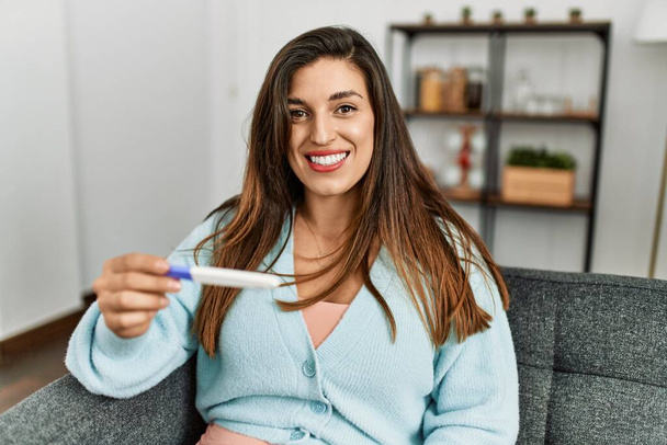 Young woman looking pregnancy test result sitting on sofa at home - Photo, Image