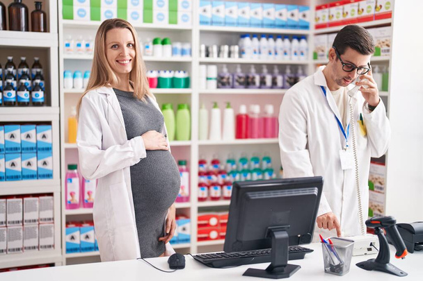 Man and woman pharmacists using computer talking on telephone at pharmacy - Photo, image