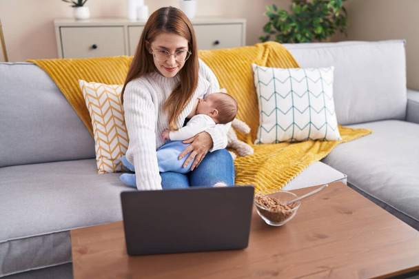 Mutter und Sohn stillen ihr Baby zu Hause mit Laptop - Foto, Bild