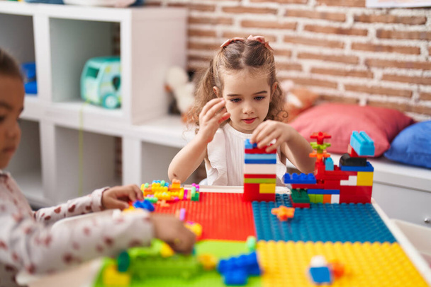 Двое детей играют со строительными блоками, сидя на столе в детском саду - Фото, изображение