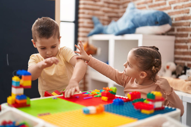 Dwoje dzieci bawiących się klockami budowlanymi siedzącymi na stole w przedszkolu - Zdjęcie, obraz