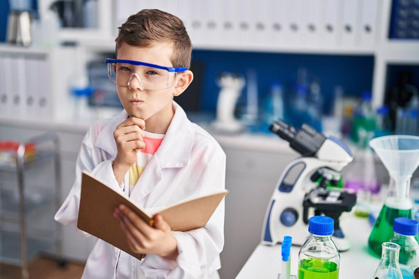 Blond child wearing scientist uniform reading book at laboratory - Foto, immagini
