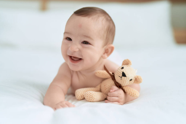 Adorable toddler lying on bed holding teddy bear at bedroom - Foto, Bild