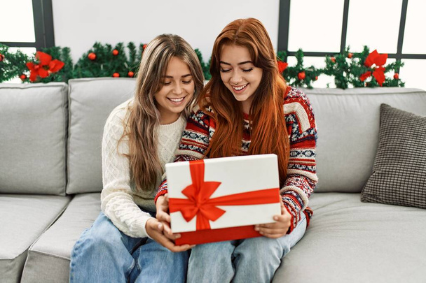 Kadın çift hediye paketini açıyor evde Noel dekorunun yanında oturuyor. - Fotoğraf, Görsel