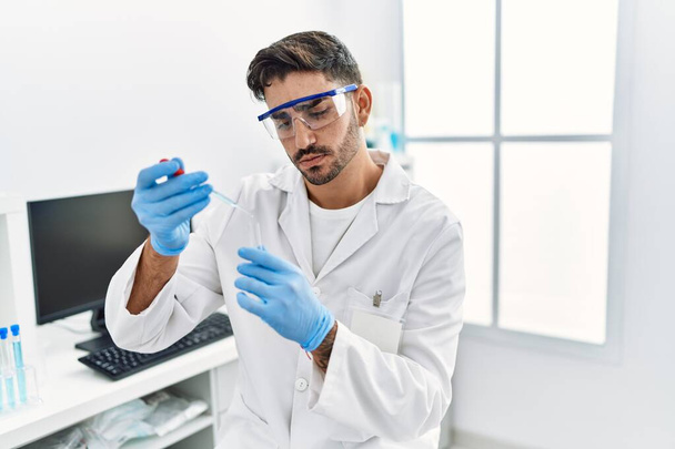 Handsome hispanic man working as scientific holding test tube at laboratory - Foto, Imagen