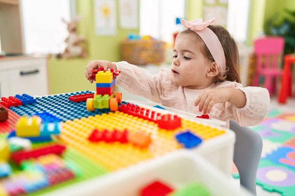Imádnivaló szőke kisbaba játszik építőkockákkal ül az asztalon az óvodában - Fotó, kép