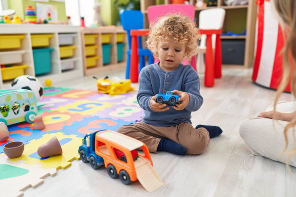 Adorable niño rubio jugando con coches juguete sentado en el suelo en el jardín de infantes - Foto, imagen