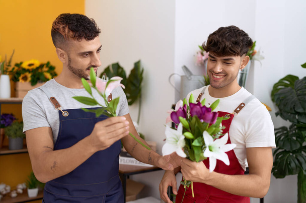 Two hispanic men florists smiling confident holding bouquet of flowers at flower shop - Fotó, kép