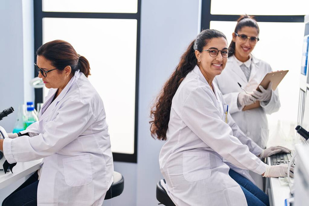 Tres científicas sosteniendo muestra escriben en lista de verificación en laboratorio - Foto, Imagen