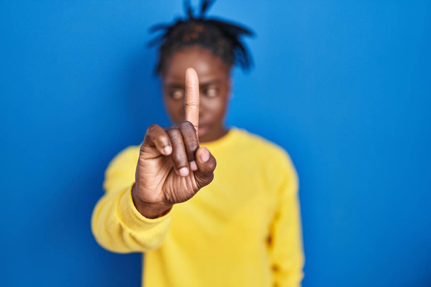 Belle femme noire debout sur fond bleu pointant avec le doigt vers le haut et l'expression en colère, ne montrant aucun geste  - Photo, image