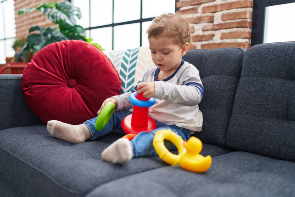 Αξιολάτρευτο καυκάσιο αγόρι παίζει με στεφάνια παιχνίδι κάθεται στον καναπέ στο σπίτι - Φωτογραφία, εικόνα