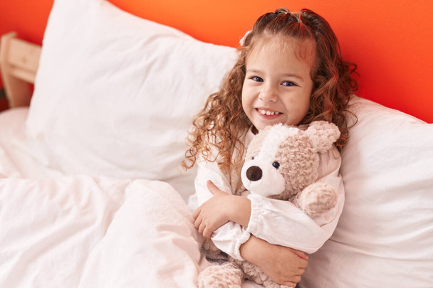 Adorável loira criança abraçando ursinho de pelúcia deitado na cama no quarto - Foto, Imagem