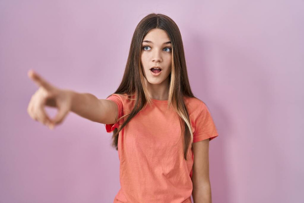 10代の女の子立ってピンクの背景を指して指で先に驚いて、口を開けて驚くような表現、何かの前に  - 写真・画像