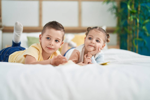 Δύο παιδιά διαβάζουν παραμύθια ξαπλωμένα στο κρεβάτι στην κρεβατοκάμαρα. - Φωτογραφία, εικόνα